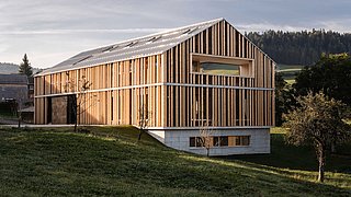 Foto, modernes Gebäude mit vertikalen Holzlatten als Fassade auf einem leicht geneigten Grundstück mit Bäumen