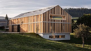 Foto, modernes Gebäude mit vertikalen Holzlatten als Fassade auf einem leicht geneigten Grundstück mit Bäumen
