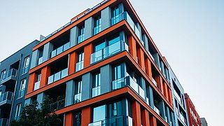 Foto, Blick hinauf an der Fassade eines mehrstöckigen Neubaus mit auffälligen roten Fassadenelementen.