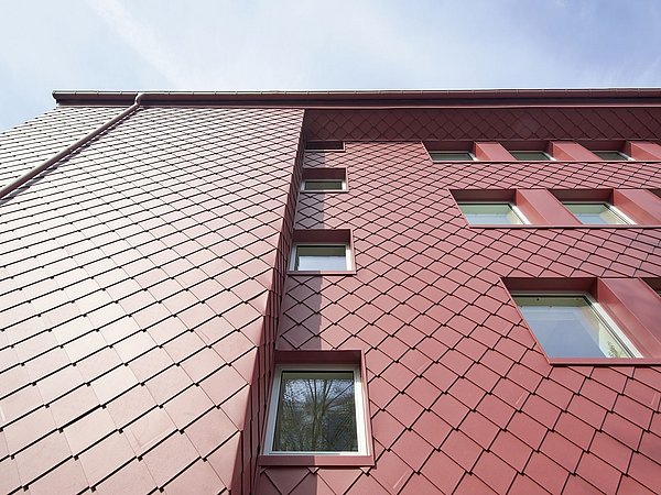Foto, Fassade eines modernen Gebäudes mit roten, schuppenartig angeordneten Metallplatten und mehreren rechteckigen Fenstern