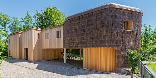 Foto, das Rosana Waldhaus mit einer mit Holz und Weidenzweigen verkleideten Fassade in organischer Form.