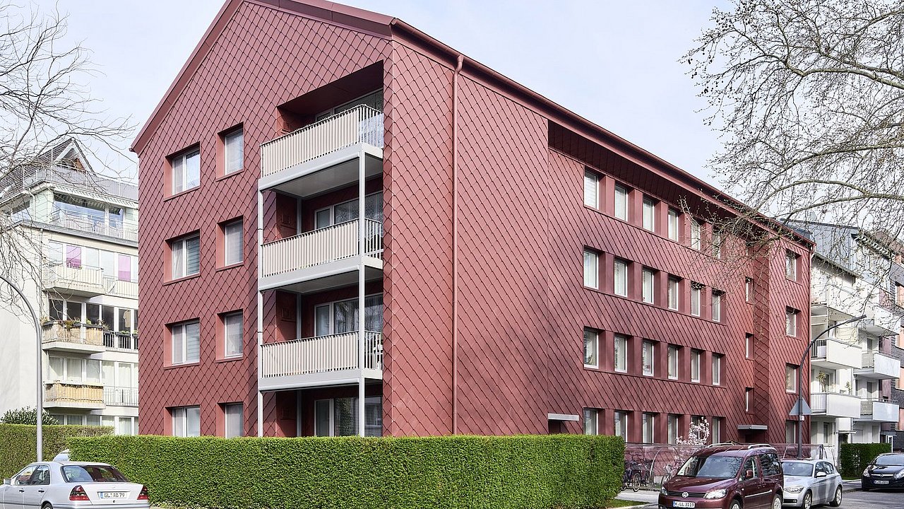 Foto, Mehrstöckiges Wohngebäude mit roter Fassade und Balkonen an einer Straßenecke