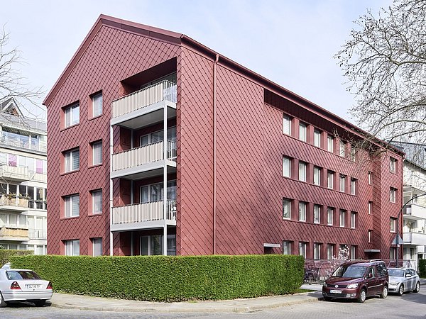 Foto, Mehrstöckiges Wohngebäude mit roter Fassade und Balkonen an einer Straßenecke