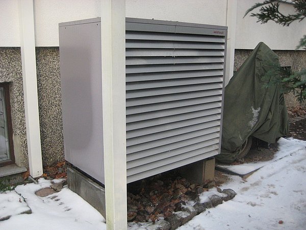 Foto, Außenansicht einer grauen Wärmepumpe neben einem Haus mit Schnee auf dem Boden