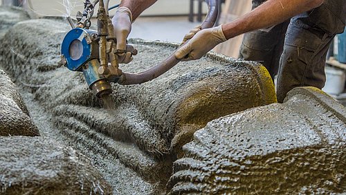 Foto, ein Arbeiter spritzt faserverstärkter Beton in mehreren Schichten in eine 3D-gedruckte Schalung.