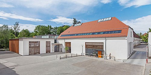 Foto, Modernes Gebäude mit rotem Satteldach und Solarpaneelen, weißer Fassade und großem Fensterfront im Eingangsbereich