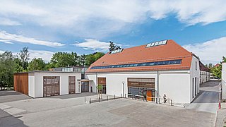 Foto, Modernes Gebäude mit rotem Satteldach und Solarpaneelen, weißer Fassade und großem Fensterfront im Eingangsbereich