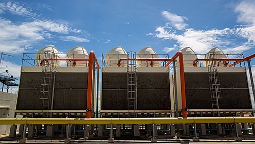 Foto, mehrere große industrielle Kühltürme mit weißen Kuppeln und orangen Rohren unter blauem Himmel.