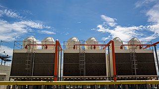 Foto, mehrere große industrielle Kühltürme mit weißen Kuppeln und orangen Rohren unter blauem Himmel.