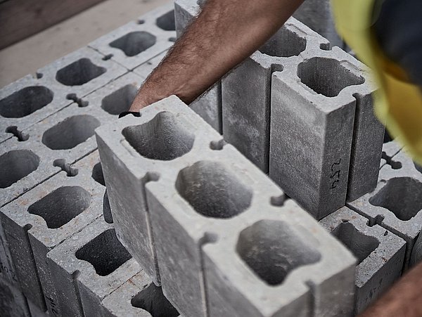 Foto, Nahaufnahme von Betonsteinen mit Hohlräumen, eine Hand greift nach einem Stein.
