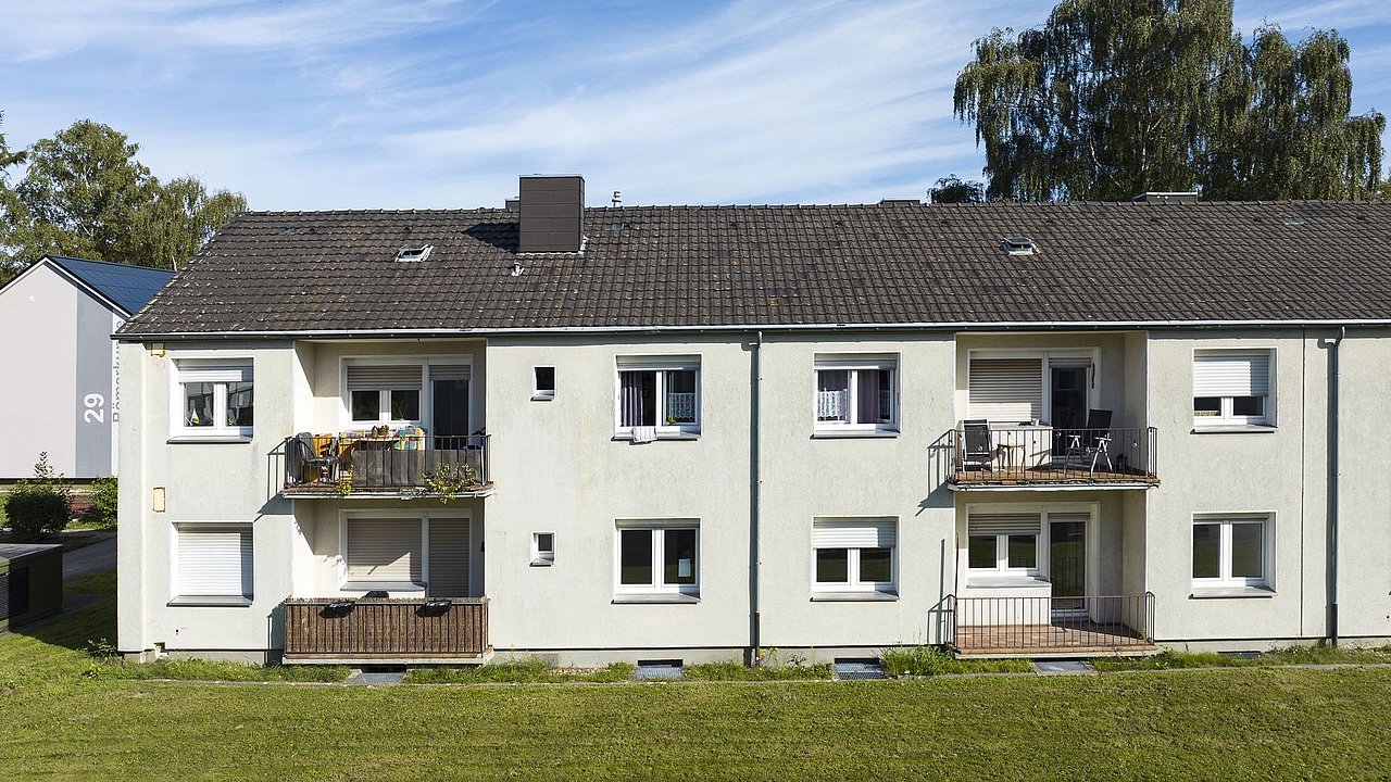 Foto, Zweistöckiges Mehrfamilienhaus mit weißen Fassaden, Balkonen und grüner Wiese im Vordergrund