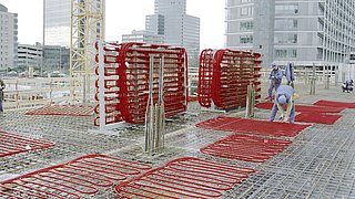 Foto, Arbeiter verlegen Rohrleitungen auf der Armierung einer neu zu gießenden Betondecke.