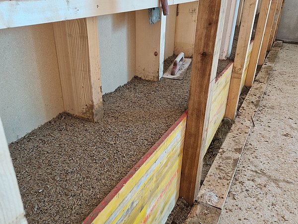 Foto, Blick auf eine mit Korkgranulat gefüllte, von Holzrahmen umgebene Boden- oder Wandkonstruktion in einem Rohbau