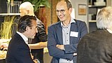 Foto, Eine Gruppe von Menschen, die sich in einem schön dekorierten Veranstaltungsraum mit Pflanzen im Hintergrund unterhalten.
