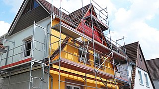 Foto, Haus mit gelber Fassade und braunem Dach mit Gerüst für Bauarbeiten.