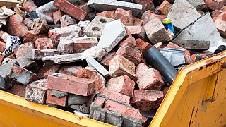 Foto, gelber Container gefüllt mit zerbrochenen Ziegelsteinen und Bauschutt.