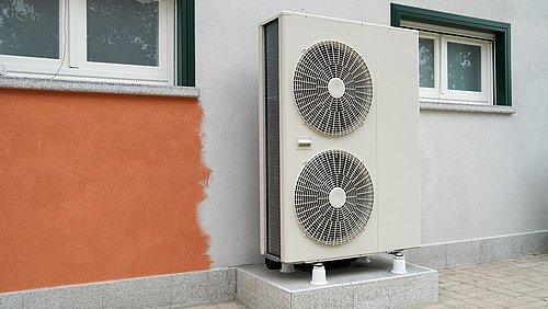 Foto, große Wärmepumpe vor einer Gebäudewand.