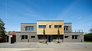 Foto, Modernes zweistöckiges Wohnhaus mit grauer Fassade und Holzverkleidung im Obergeschoss, zwei junge Bäume davor