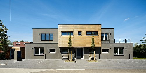 Foto, Modernes zweistöckiges Wohnhaus mit grauer Fassade und Holzverkleidung im Obergeschoss, zwei junge Bäume davor