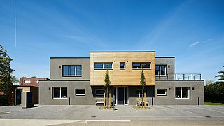 Foto, Modernes zweistöckiges Wohnhaus mit grauer Fassade und Holzverkleidung im Obergeschoss, zwei junge Bäume davor