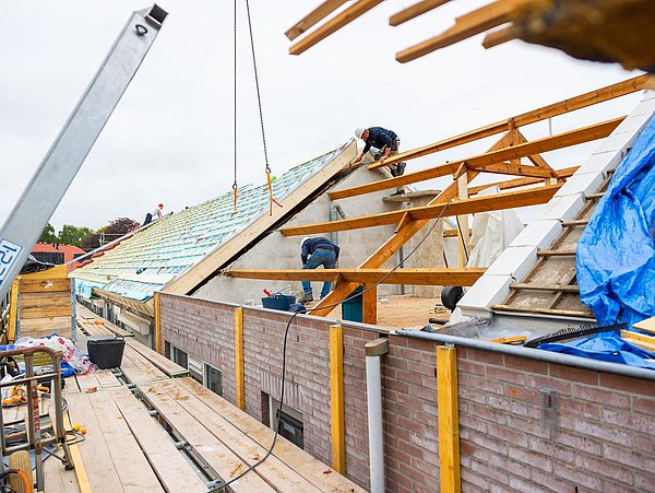 Foto, Bauarbeiter auf einem Dachstuhl mit Holzkonstruktionen und blauer Abdeckung.