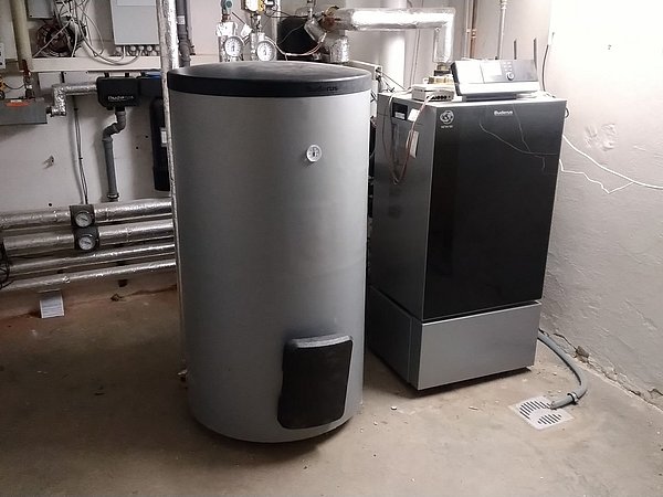 Foto, Großer zylindrischer Warmwasserspeicher neben einer Heizungsanlage in einem Kellerraum