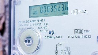 Foto, Nahaufnahme eines digitalen Stromzählers mit Display, Drehknopf und technischen Beschriftungen.