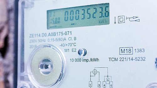 Foto, Nahaufnahme eines digitalen Stromzählers mit Display, Drehknopf und technischen Beschriftungen.