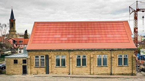 Foto, eine Kirche mit einem Solardach aus rot eingefärbten Modulen.