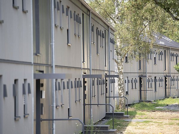 Foto, Reihen von zweistöckigen Wohngebäuden mit weißen Fassaden und kleinen Fenstern, umgeben von Bäumen und Gras
