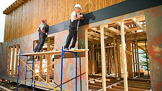 Foto, zwei Handwerker arbeiten an der Fassade eines Neubaus aus Holz.