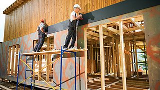 Foto, zwei Handwerker arbeiten an der Fassade eines Neubaus aus Holz.