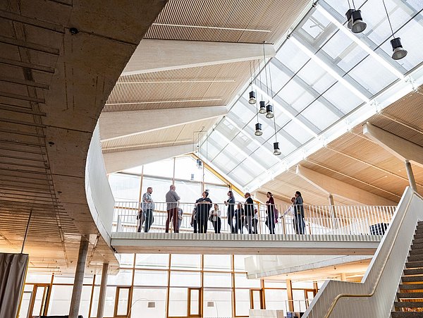 Foto, moderner Innenraum aus Holz und Glas in dem Personen auf einer Brücke stehen.