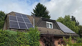 Foto, Dach mit Photovoltaikanlage und Teile der Klinkerfassade eines Einfamilienhauses, das hinter Begrünung steht