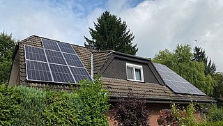 Foto, Dach mit Photovoltaikanlage und Teile der Klinkerfassade eines Einfamilienhauses, das hinter Begrünung steht