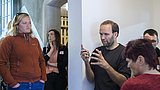Foto, Gruppe von Menschen in einem Raum, eine Person gestikuliert mit den Händen, andere hören zu