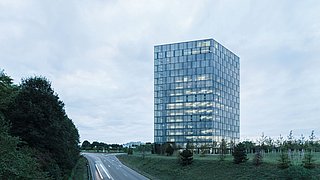 Foto, eine Straße mit Begrünung zu beiden Seiten. Rechts von der Straße befindet sich ein Hochaus mit Glasfassade.