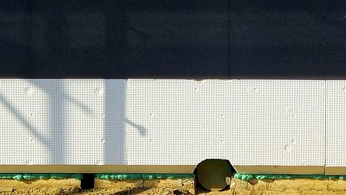 Foto, Nahaufnahme einer weißen Perimeterdämmung mit sichtbarer Struktur und Schattenwurf an einer dunklen Wand.