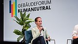 Foto, ein Frau sitzt auf einem Stuhl auf einer Bühne und spricht in ein Mikrofon.