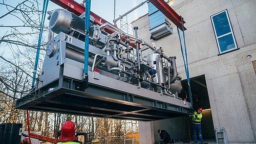 Foto, eine Großwärmepumpe wird per Kran angeliefert.
