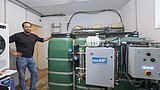 Foto, Mann lehnt an grünem Industrietank mit angeschlossener technischer Anlage in einem Raum