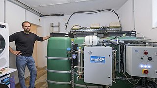 Foto, Mann lehnt an grünem Industrietank mit angeschlossener technischer Anlage in einem Raum