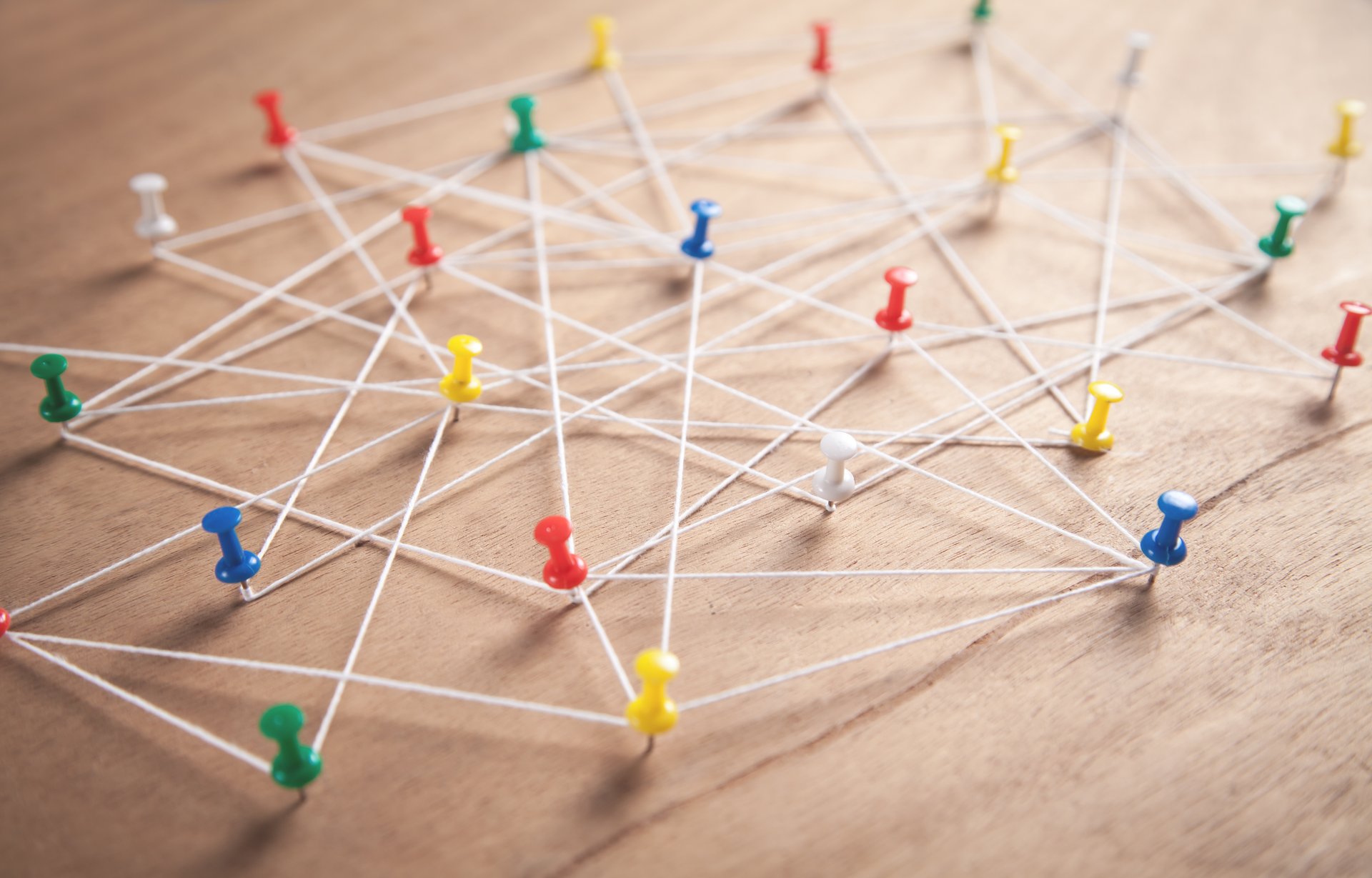 Foto, Nahaufnahme von mehreren Stecknadeln in einer Pinwand, die mit Bindfäden untereinander verbunden sind.