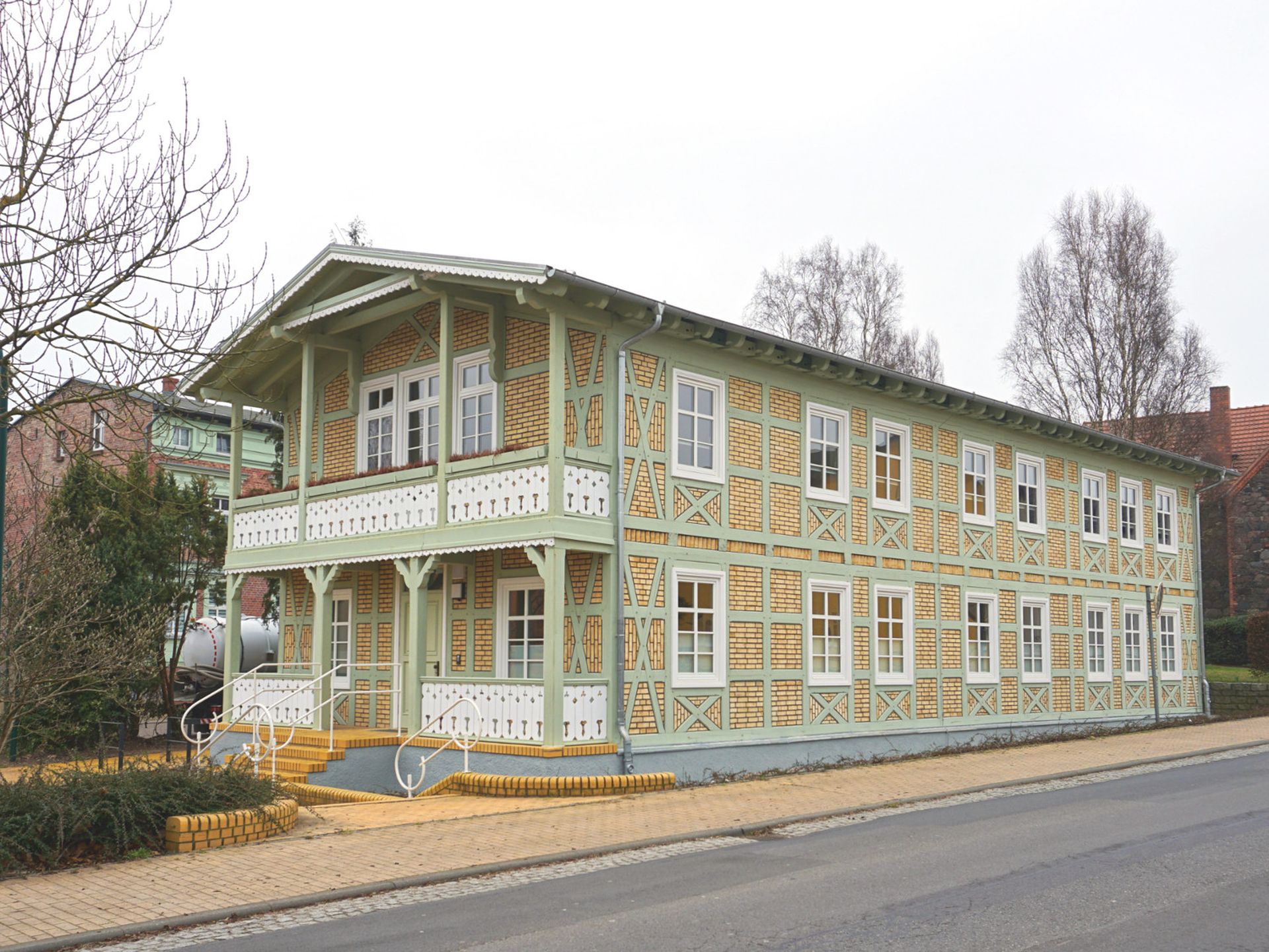 Foto, Zweistöckiges Fachwerkhaus mit gelben Ziegeln und grünen Holzbalken an einer Straße