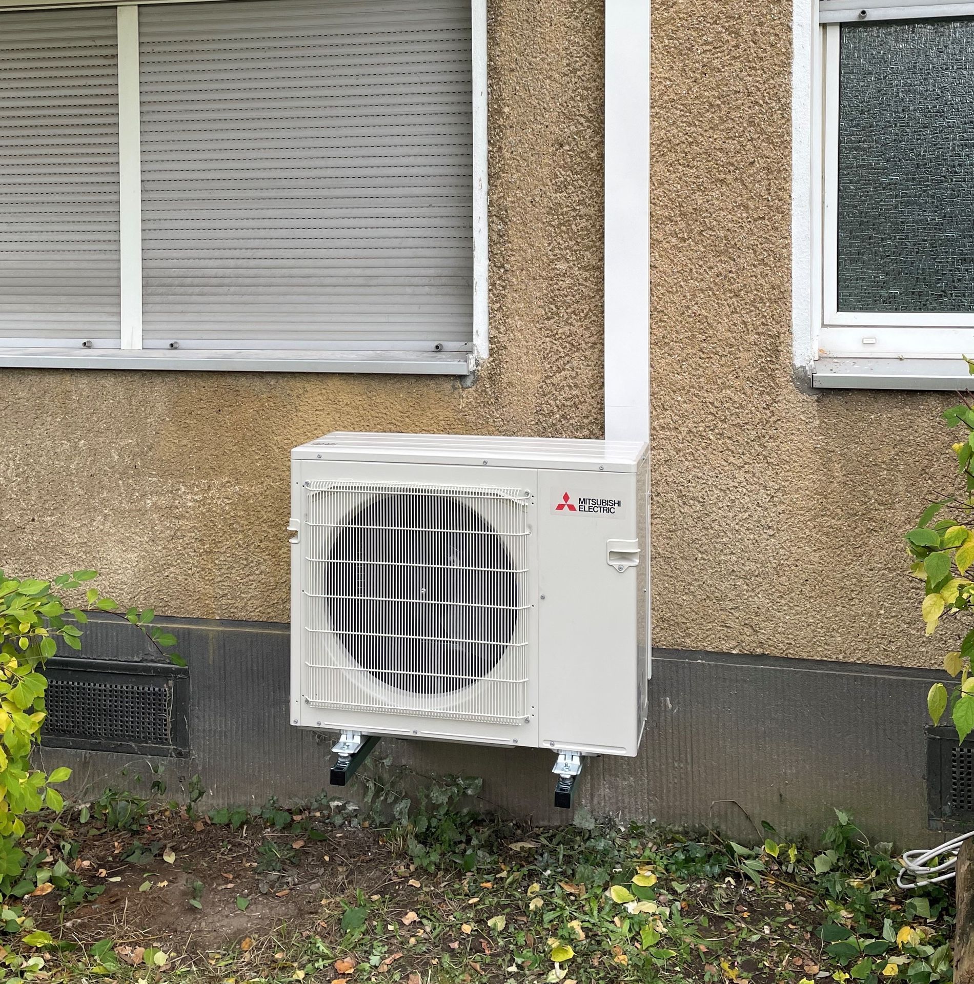 Foto, Außeneinheit einer Wärmepumpe an der Fassade eines Gebäudes mit zwei Fenstern