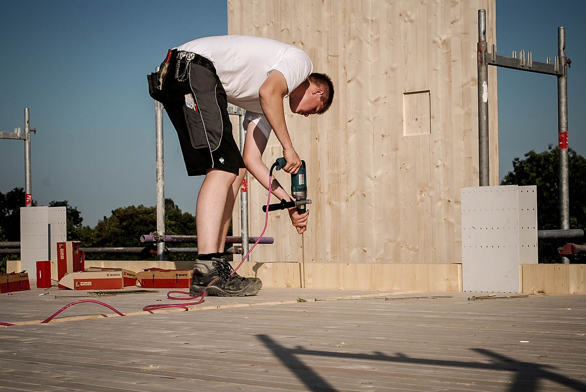 Foto, eine Person in Arbeitskleidung bohrt auf einer Baustelle in den Fußboden.