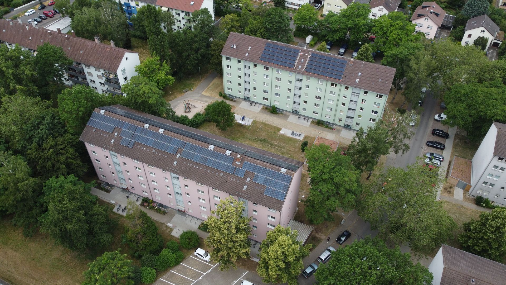 Foto, Mehrfamilienhäuser mit Solaranlagen auf den Dächern, umgeben von Bäumen und Parkplätzen in einem Wohngebiet