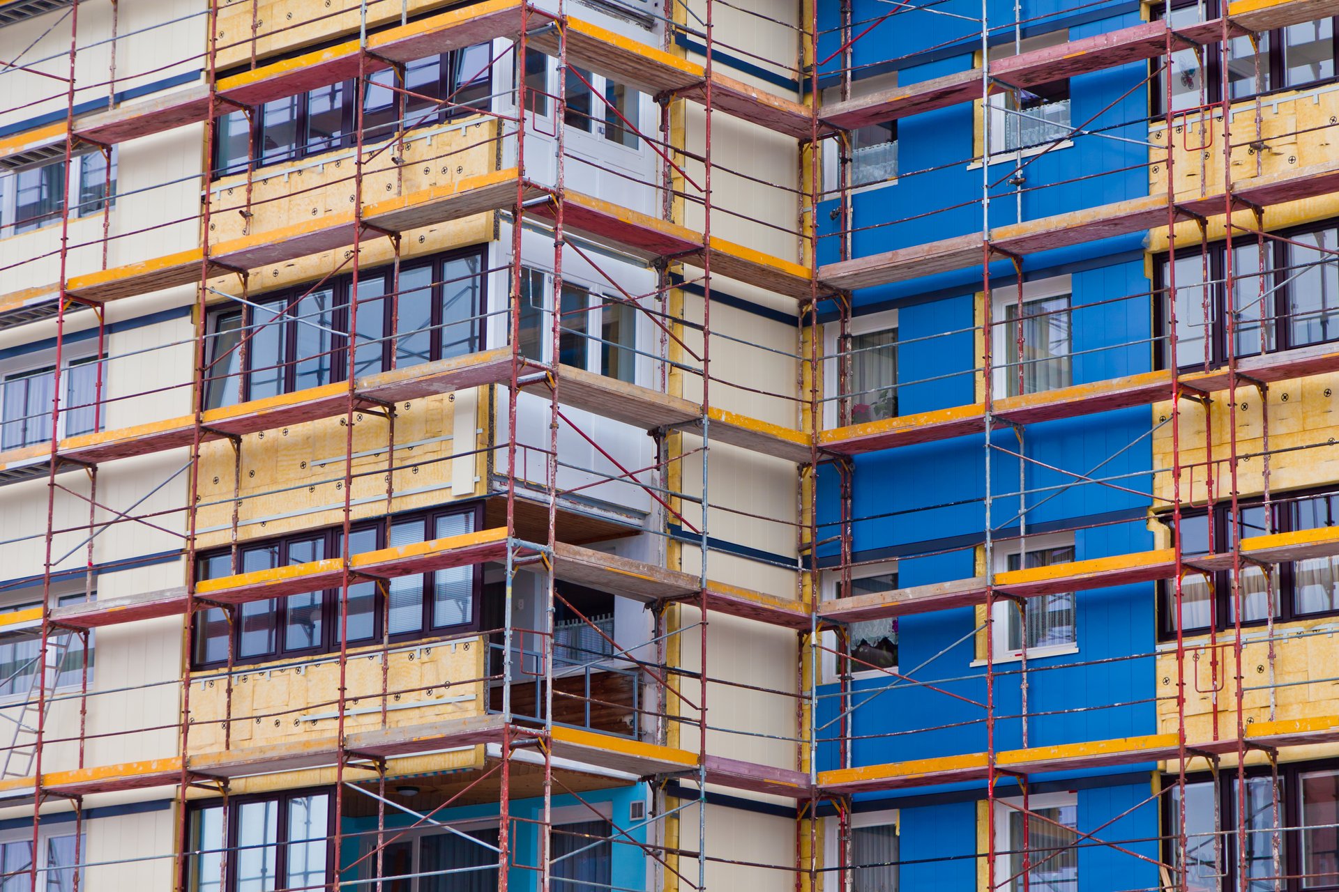 Foto, Nahaufnahme eines mehrstöckigen Wohngebäudes mit Baugerüst, bei dem die Fassade gedämmt wird.