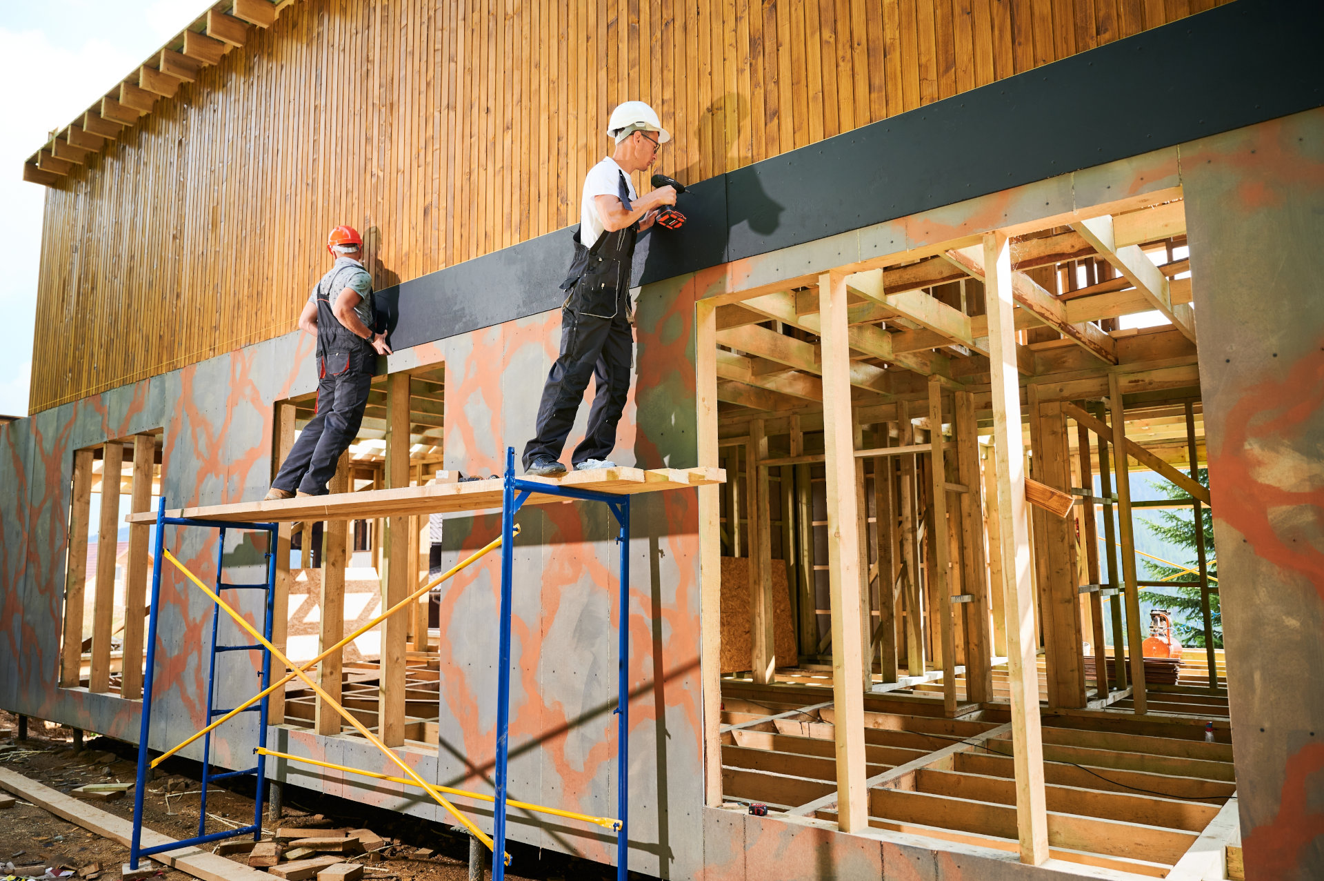 Foto, zwei Handwerker arbeiten an der Fassade eines Neubaus aus Holz.