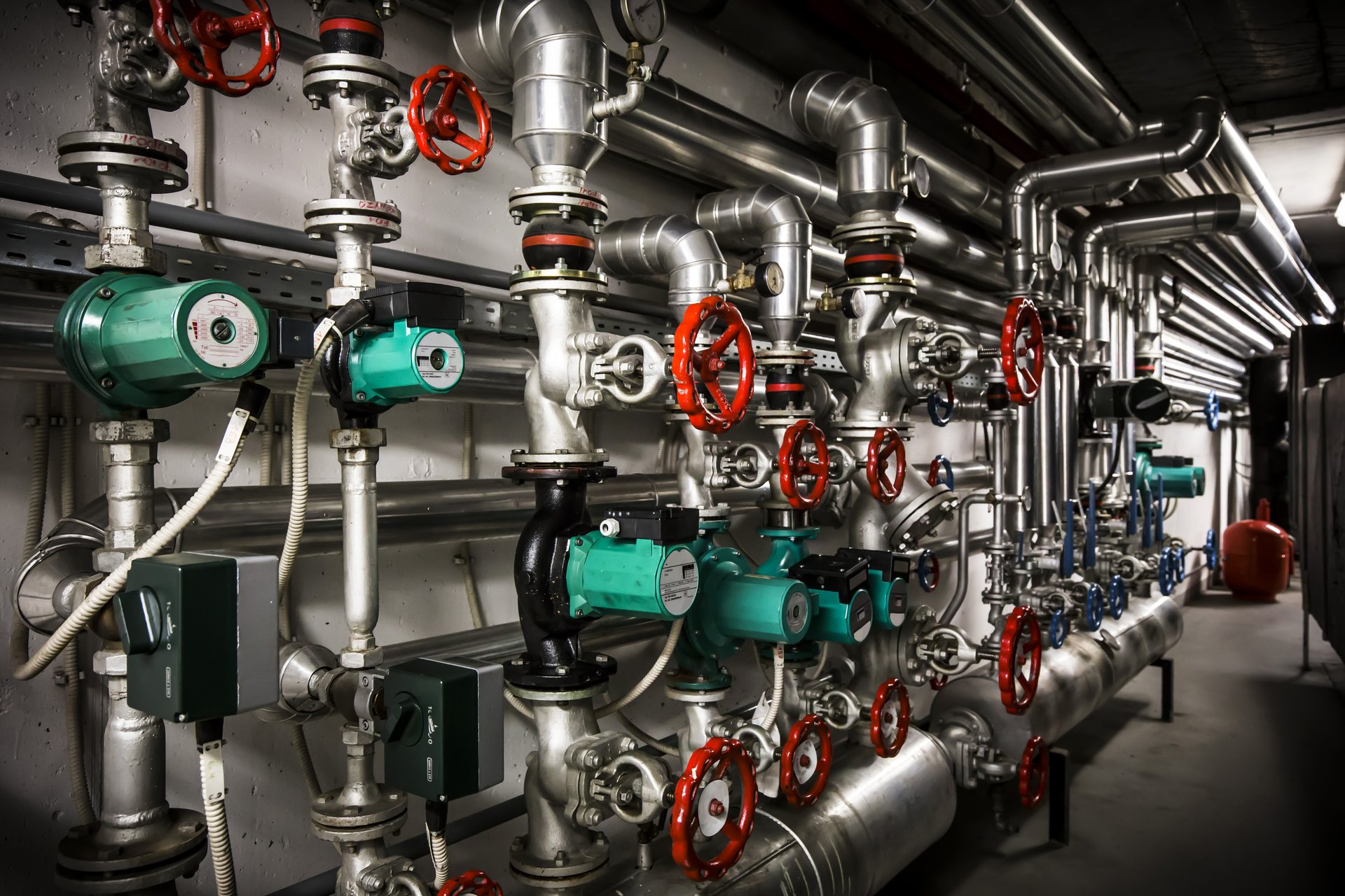 Foto, Aufnahme eines Geflechts von wandmontierten Rohrleitungen sowie von Heizungspumpen und Sperrventilen.